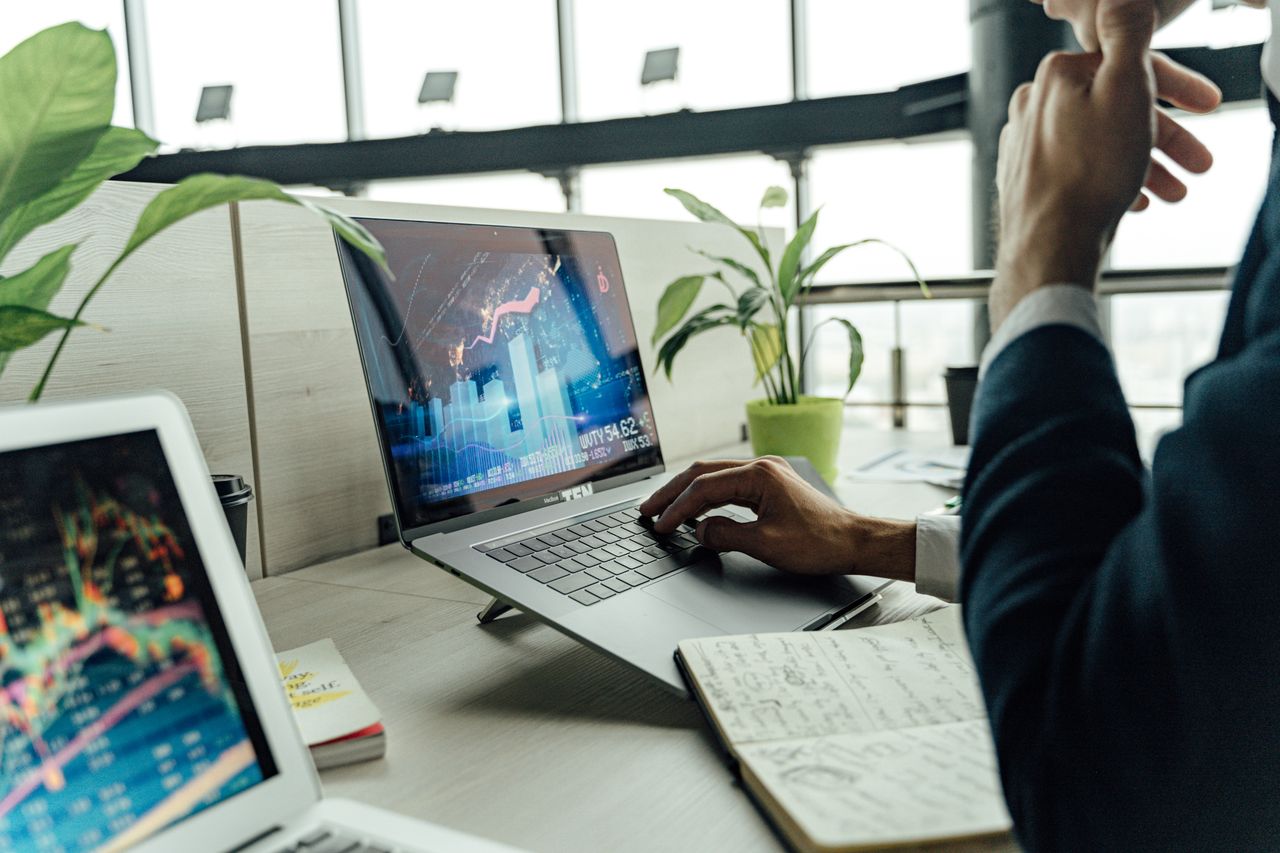 Home A professional analyzing stock market data on a laptop in a bright office environment.